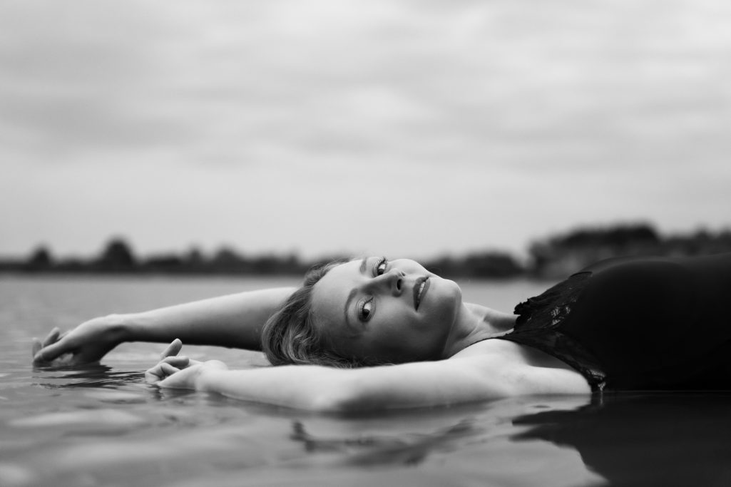 Frau liegt entspannt im Wasser, Blick in die Kamera, Schwarz-Weiß-Fotografie.