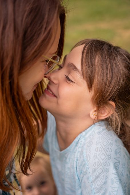 Eine Frau und ein Mädchen lächeln sich liebevoll an, im Hintergrund ein weiteres Kind.
