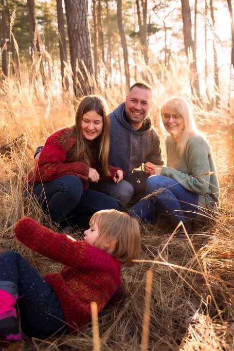 Eine Familie sitzt im Gras und spielt zusammen in einem sonnigen Wald.