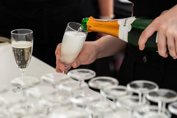 Eine Hand gießt Sekt in ein Glas, darunter stehen weitere Gläser.