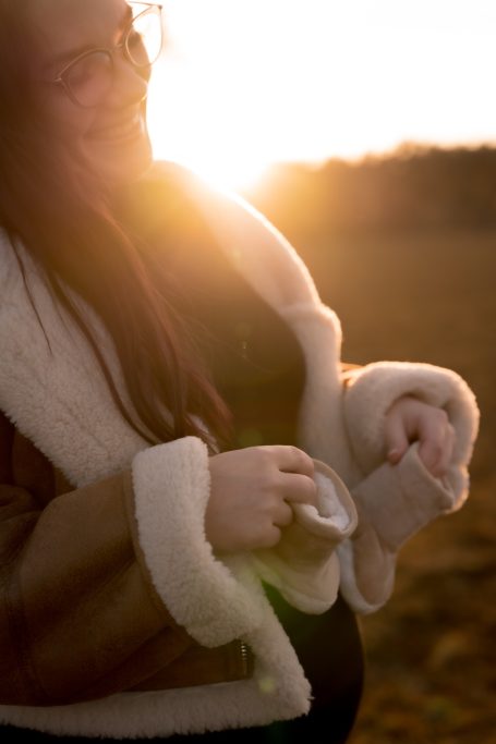 Eine lächelnde Person in einem hellen, natürlichen Umfeld mit Sonnenuntergang im Hintergrund.