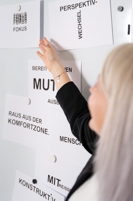 Eine Person weist auf ein Plakat mit Worten wie "Mut" und "Perspektive".