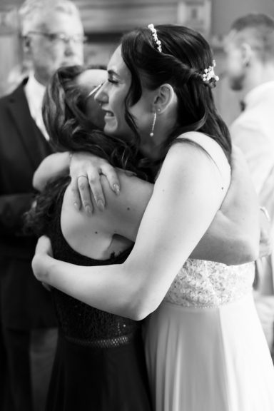Zwei Frauen umarmen sich liebevoll bei einer Feier. Eine trägt ein Brautkleid.