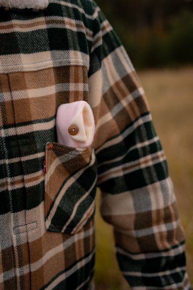 Person in kariertem Hemd mit rosa Objekt in der Brusttasche.