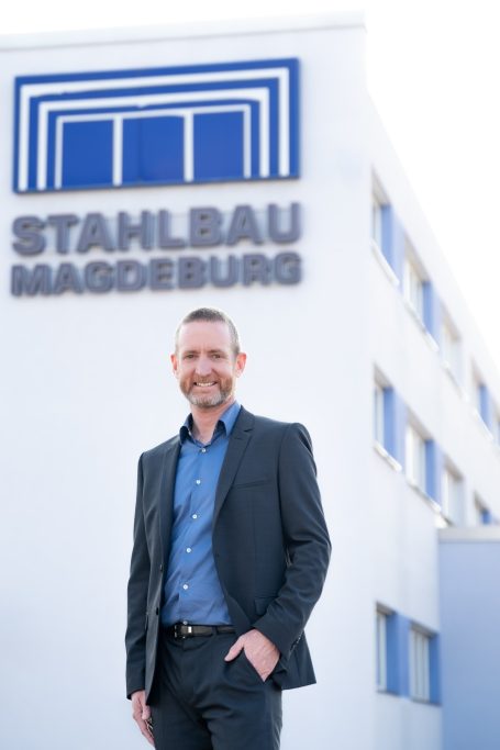 Mann in Anzug steht lächelnd vor der Stahlbau Magdeburg-Firma.