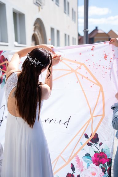 Frau in weißem Kleid hält ein Banner mit einem geometrischen Muster und floralem Design.