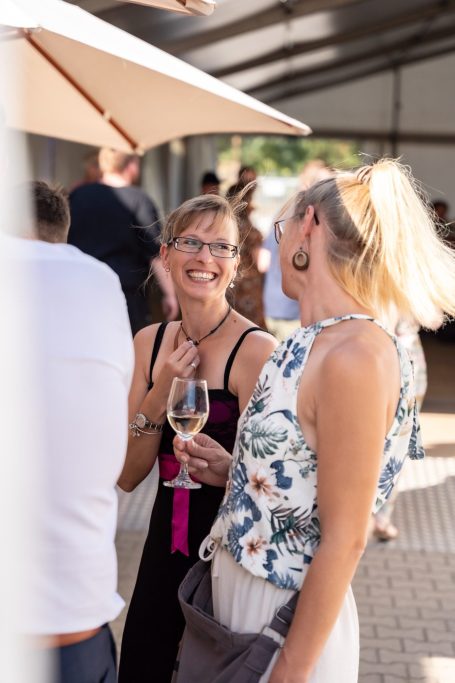 Zwei Frauen lachen und unterhalten sich, eine hält ein Weinglas in der Hand.