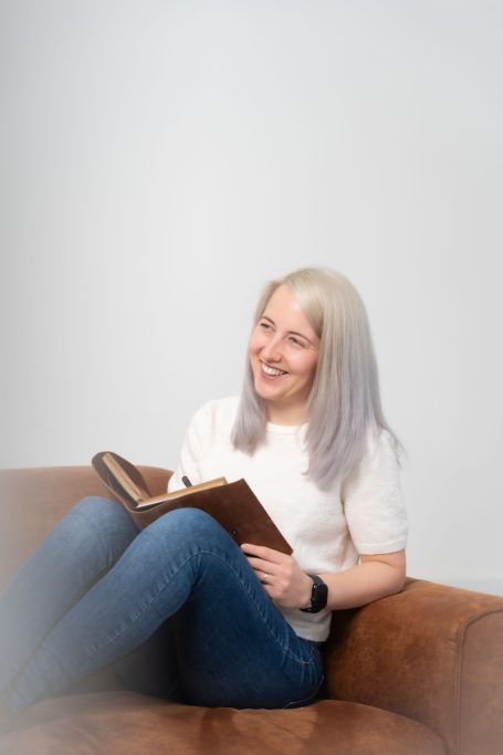 Frau mit blonden Haaren sitzt auf einer Couch und liest in einem Buch.
