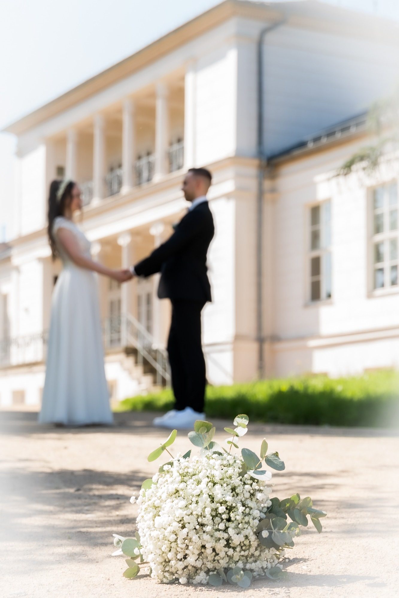 Hochzeitspaar geht Hand in Hand auf einem Weg, umgeben von Bäumen.