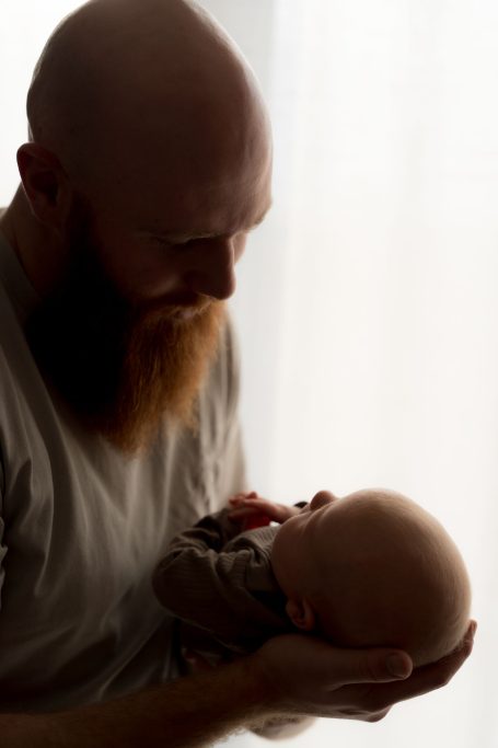 Ein Vater hält sein Neugeborenes sanft in den Händen, beide schauen sich an.