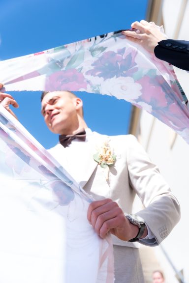 Ein lächelnder Mann in einem Anzug hält einen bunten Stoff im Freien.