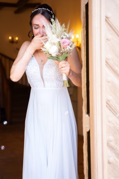 Braut in einem weißen Kleid, wischte sich Tränen weg und hält einen Blumenstrauß.
