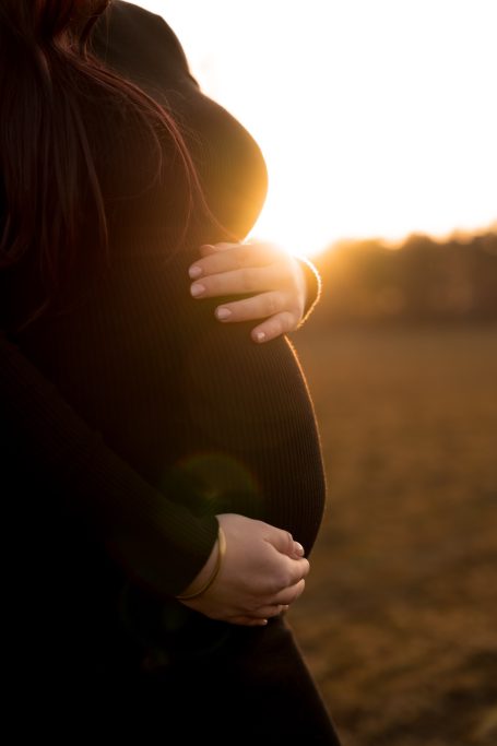 Schwangere Frau hält ihren Bauch bei Sonnenuntergang in einer natürlichen Umgebung.
