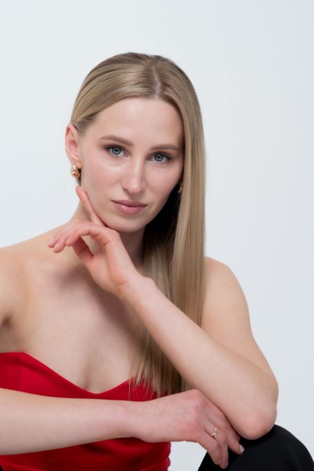 Porträt einer Frau mit langen blonden Haaren, die in einem roten Oberteil posiert.