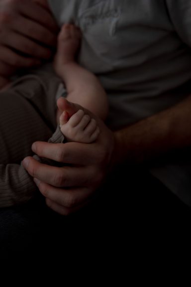 Hände halten einen kleinen Fuß eines Babys, sanfte und liebevolle Umarmung.