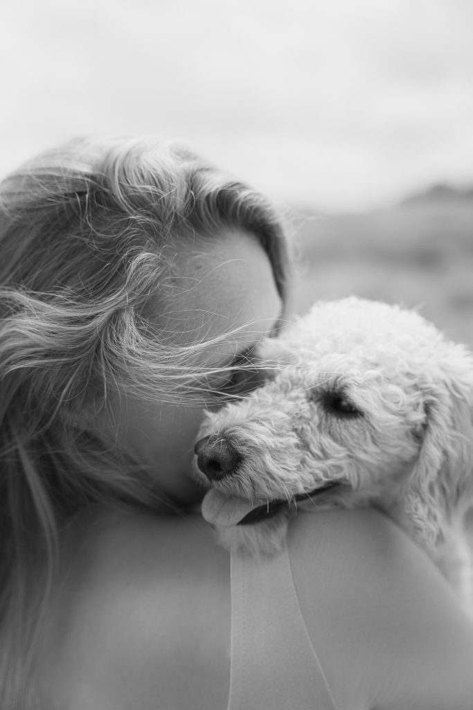 Frau kuschelt mit einem weißen Hund auf einem verschwommenen Hintergrund.