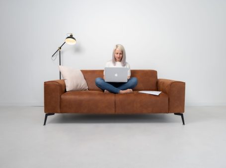 Eine Frau sitzt auf einem braunen Sofa und arbeitet am Laptop.