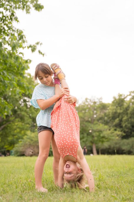 Zwei Kinder spielen im Freien, eines macht Handstand, das andere hält es fest.