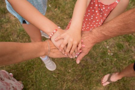 Hände von Erwachsenen und Kindern, die übereinander auf Rasen liegen.