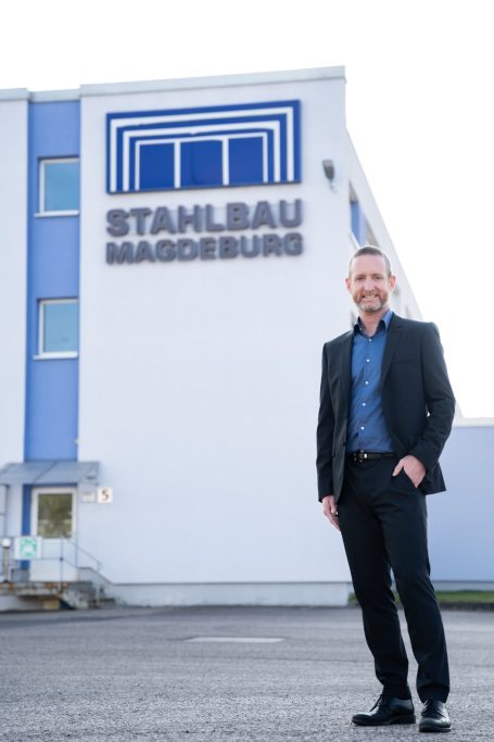 Mann in Anzug steht vor dem Gebäude der Firma Stahlbau Magdeburg.
