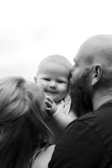 Ein Happy Baby wird von seinen Eltern liebevoll umarmt und geküsst.
